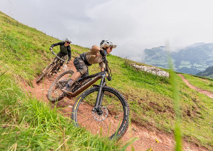 Mountainbiker fahren durch eine enge Kurve auf einem Naturtrail am Berghang.