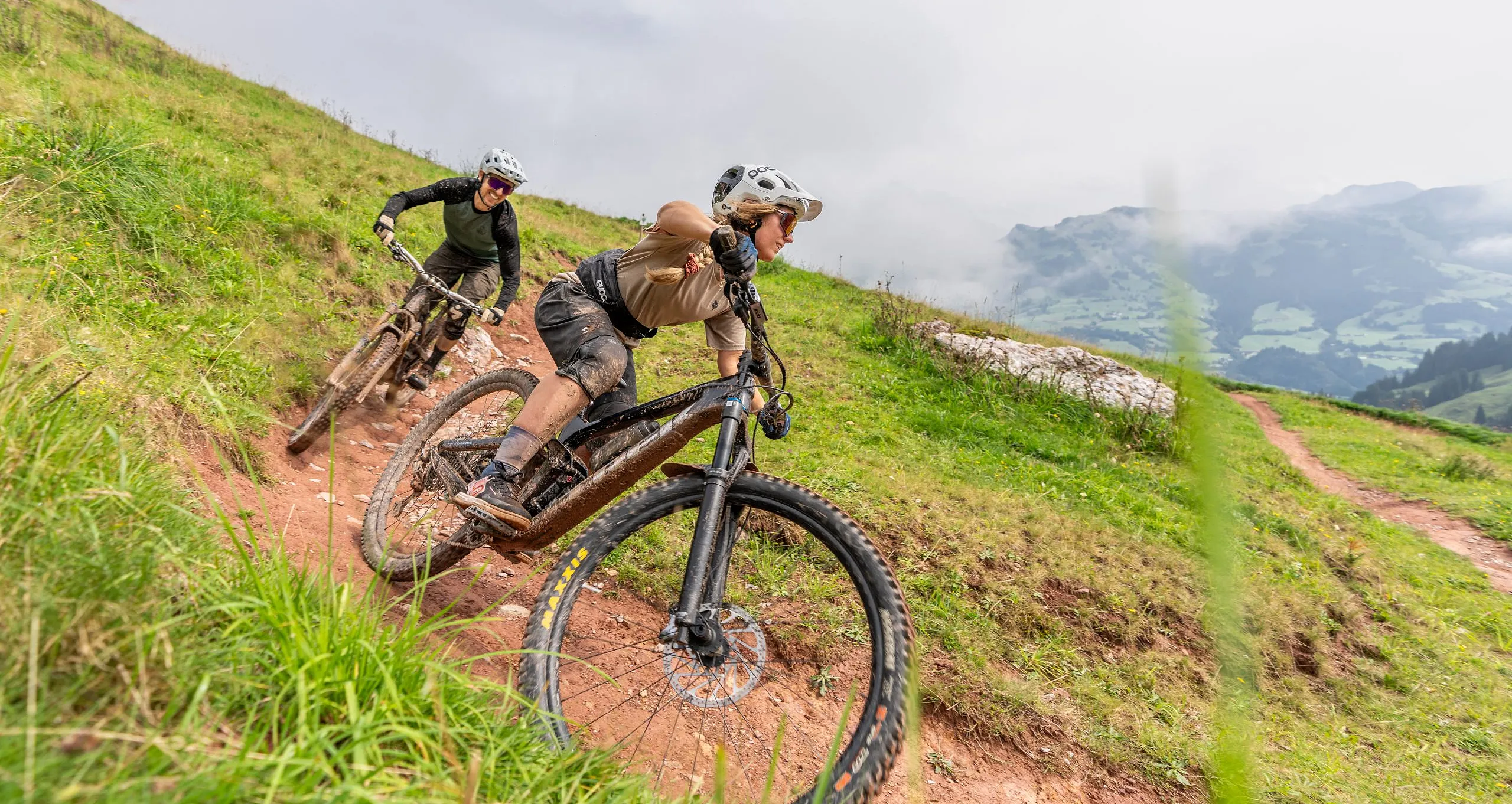 Zwei Mountainbiker stehen an einem Aussichtspunkt mit Bergpanorama im Hintergrund.