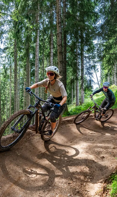 Zwei Mountainbiker fahren auf einem schmalen Trail durch die Berglandschaft der Kitzbüheler Alpen.